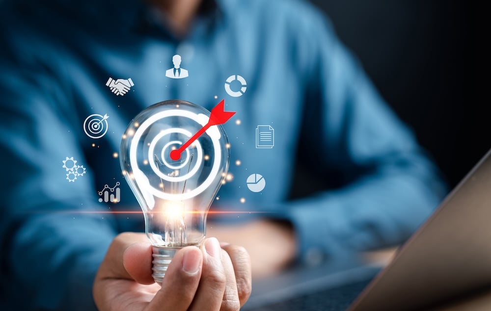 Hand holding lightbulb with icons suggesting ideas and progress